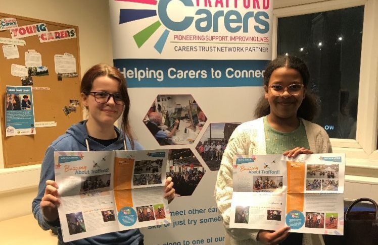 Two young carers hold up our newsletter in front of a banner