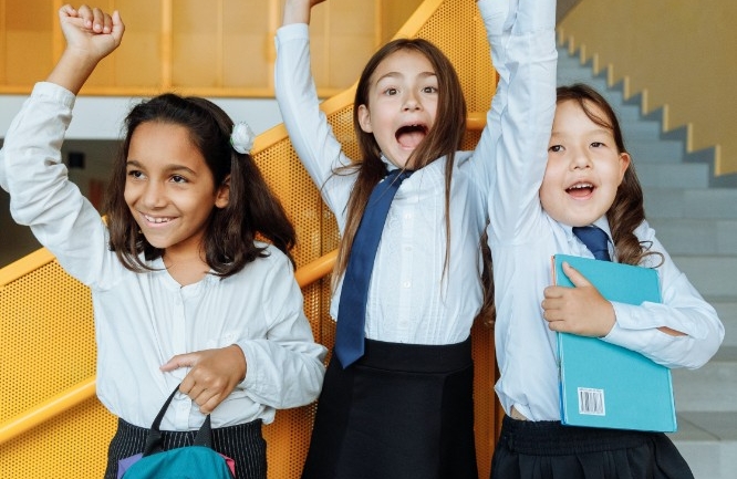 Girls cheering at school in their school uniforms holding school books