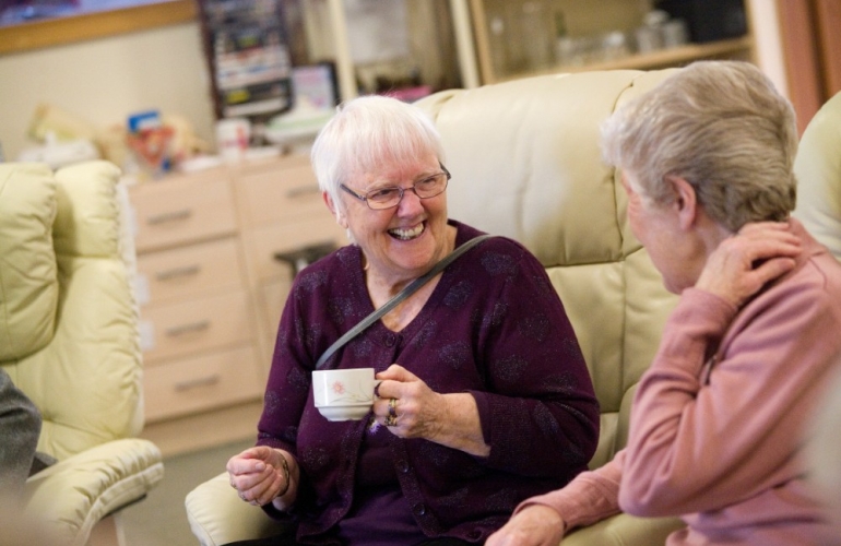 Woman smiling drinking a cup of tea with her friend