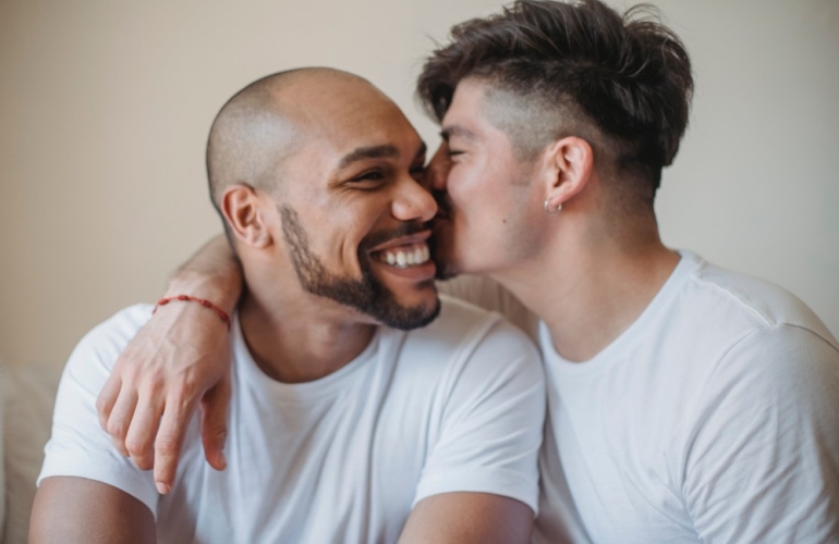 Two men smiling with a kiss on the cheek