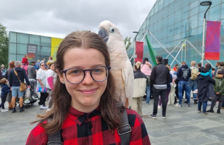 Kirsty, young carer, with parrot on shoulder next to Manchester Football Museum