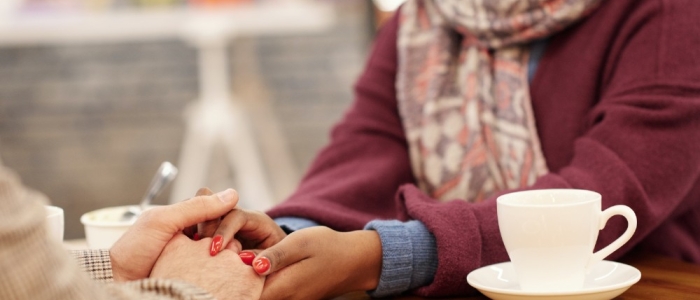 Holding someones hand on the table over cake and cup of tea