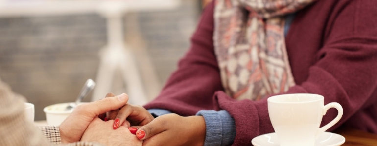 Holding someones hand on the table over cake and cup of tea